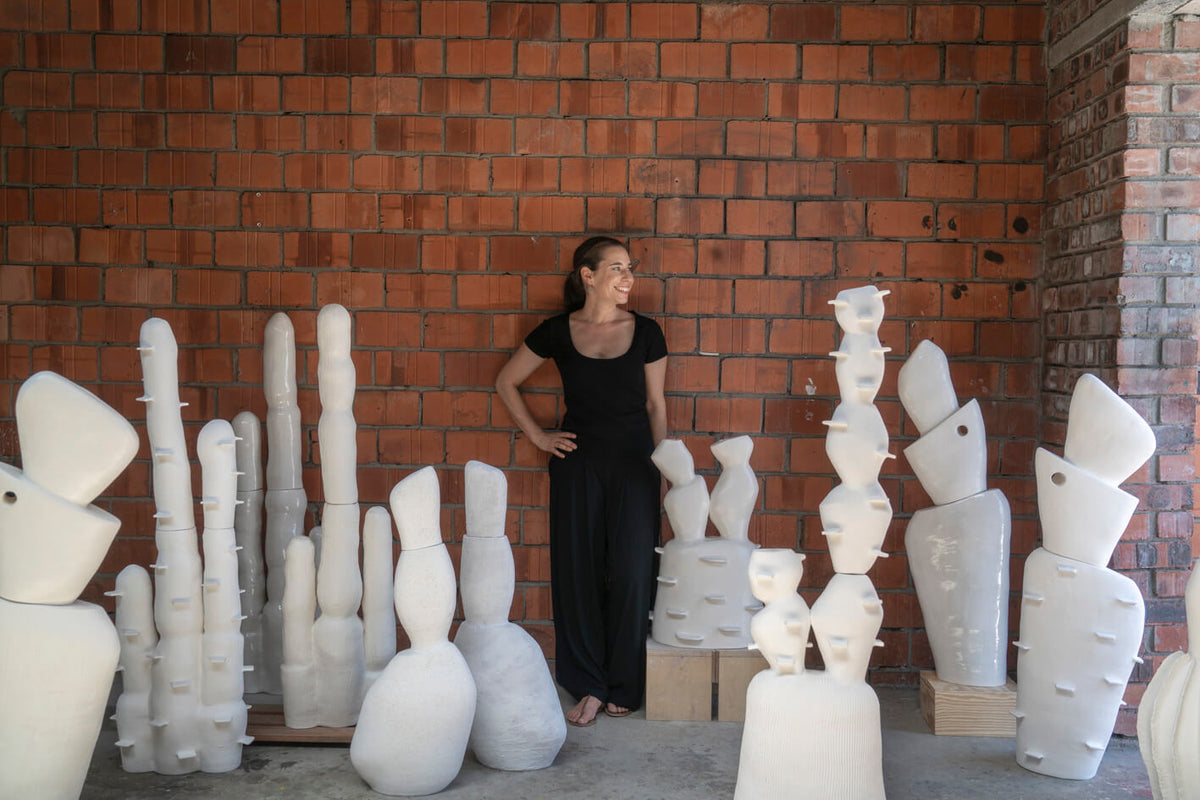 Woman standing among white ceramic sculptures against a brick wall.